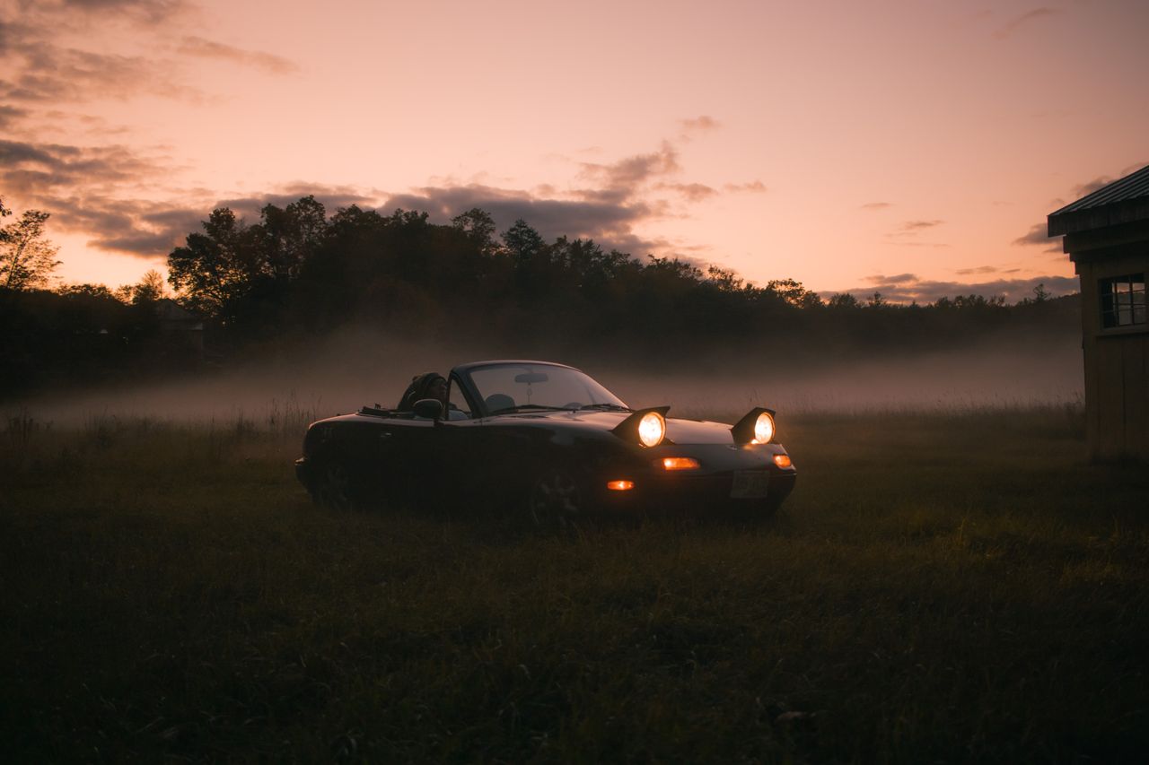 Mastering the First Impression: Your intriguing post title goes here A sports car with headlights on parked in a grassy field during a foggy sunset.